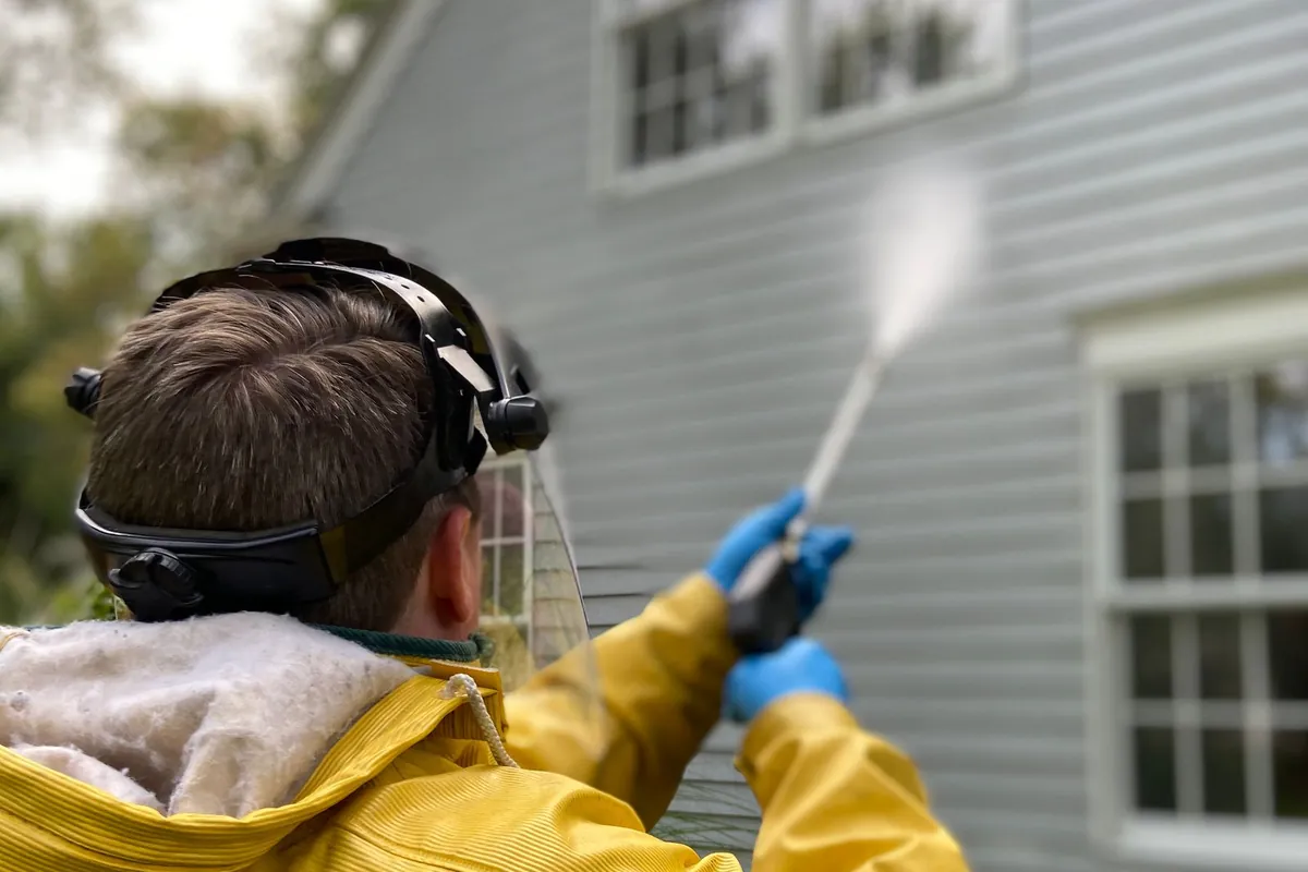 Soft washing the exterior siding of a two-story home with low-pressure equipment